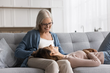 Obraz premium Older 65s pensioner woman enjoy time and pleasant talk with grown up young adult daughter, lying on loving moms knees smile lead trustworthy conversation during her visit at caring mums house. Support