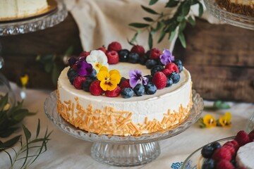 Decorated Cheesecake with Fresh Berries and Edible Flowers on a Wooden Table with Other Desserts