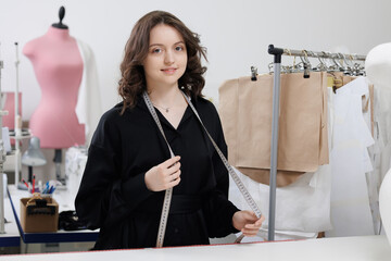 Fashion tailor woman working on clothes in tailoring atelier. Young female designer smile in studio...