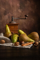 Top view of pears on cloth on table with nuts, knife and grinder, dark background, vertical, with copy space