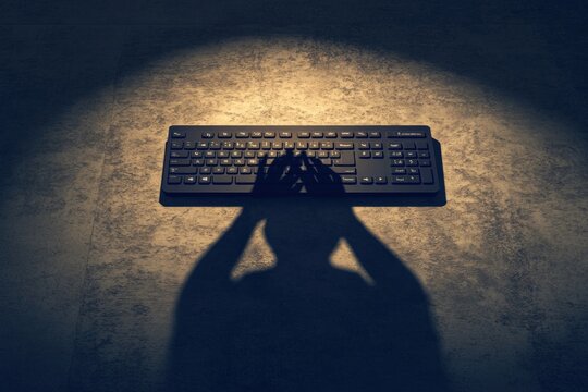 A shadowy figure with hands raised above a keyboard, creating a dramatic and mysterious scene.
