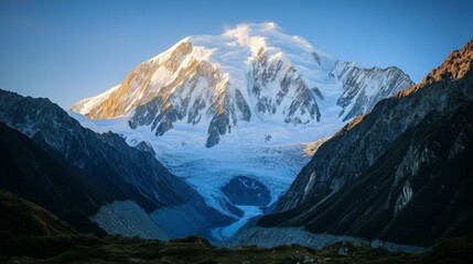 Obraz premium Majestic Snow-Capped Mountain Peak Surrounded by Vibrant Green Valley and Glacial River under Clear Blue Sky during Golden Hour Light in Stunning Landscape