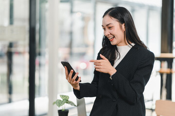 Fototapeta premium woman in black suit smiles while using her smartphone in modern office. Her joyful expression reflects engagement and excitement