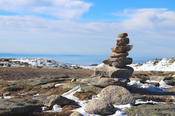 Zen stones balanced on snowy terrain, with a clear blue sky and a few clouds in the background