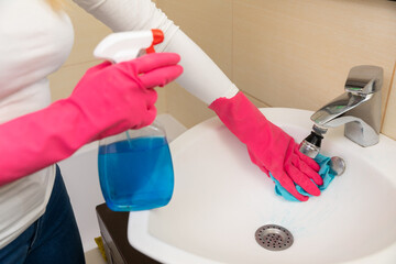 A woman is cleaning the bathroom sink with spray cleaner for hygiene and freshness