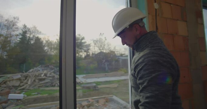 Construction worker in hard hat checks window installation on residential site, focusing on precision and alignment for quality assurance