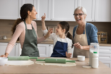 Fototapeta premium Multigenerational family, grandma, daughter and grandkid having fun while cooking together in kitchen, wearing aprons, joyfully baking, preparing food, exude love, creating memories across generations