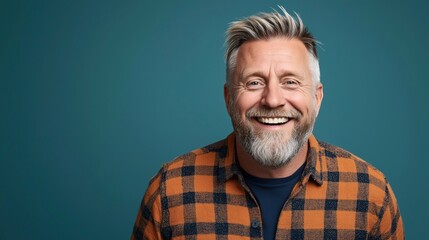 Obraz premium Smiling middle-aged man with gray hair and beard wearing a plaid shirt against a teal background in a studio setting