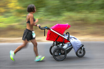 mother athlete runs in city park with baby stroller