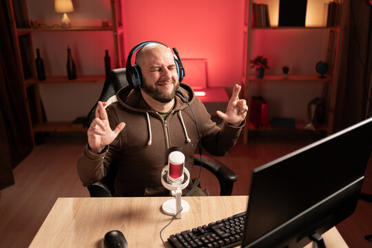 Bearded gamer man streaming and playing video games wearing headphones gesturing finger crossed. luck and superstitious - Powered by Adobe