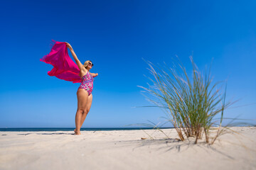 Summertime on beach. Beautiful young woman with long blond hair in colorful pink swimsuit standing...