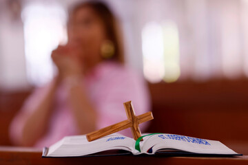 Catholic woman praying in a church. Bible and christian cross.