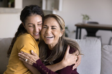 Happy retired older Latin mother and young adult daughter tightening each other with closed eyes,...