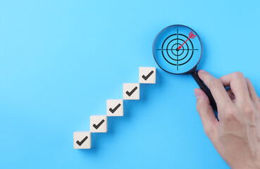 Goal Achievement Steps and Target Concept. Wooden blocks with checkmarks forming a staircase toward...