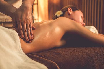 Fototapeta premium Caucasian woman customer enjoying relaxing anti-stress spa massage and pampering with beauty skin recreation leisure in warm candle lighting ambient salon spa at luxury resort or hotel. Quiescent