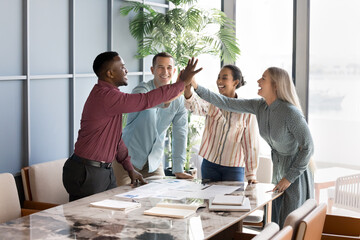 Cheerful successful multiethnic business team of young colleagues giving group high five due to...