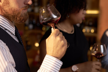 Medium close up of unrecognizable male sommeliers holding crystal glass of wine in hand while...