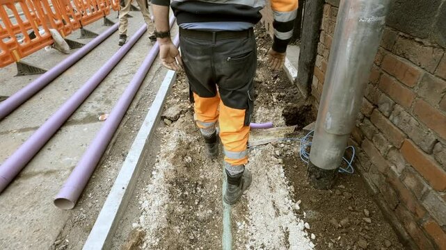 Construction worker digs up ground while installing new telecom internet duct near a building on a sunny day in the city
