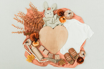 A cozy flat lay featuring a baby bodysuit, pumpkins, leaves, and rustic fall decor. Perfect for...