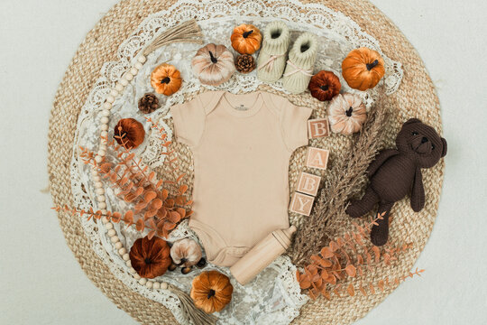 A cozy flat lay featuring a baby bodysuit, pumpkins, leaves, and rustic fall decor. Perfect for pregnancy announcements, autumn themes, and family designs.