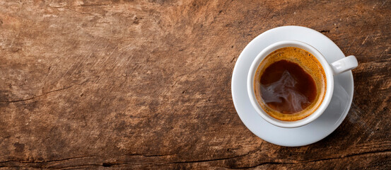 Banner or background of a hot coffee cup on a saucer viewed from above, placed to one side on an old, rustic wooden surface with copy space. Concept of natural product with rich aroma and flavor
