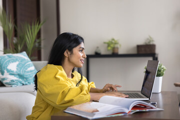 Positive young adult Indian student woman using computer for remote studying from home, watching...