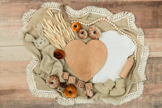 A cozy flat lay featuring a baby bodysuit, pumpkins, leaves, and rustic fall decor. Perfect for pregnancy announcements, autumn themes, and family designs.