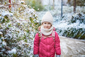 Adorable preschooler girl having fun in beautiful winter park on a snowy cold winter day