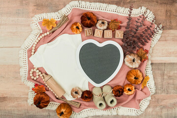 A cozy flat lay featuring a baby bodysuit, pumpkins, leaves, and rustic fall decor. Perfect for pregnancy announcements, autumn themes, and family designs.