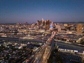 Fototapeta premium Aerial view of Los Angeles downtown at night, with the traffic on the freeway feeding into the city. Skyline lit up by urban lights.