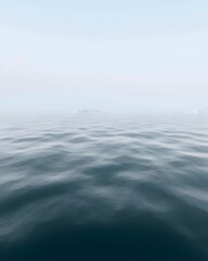 Obraz premium A serene seascape featuring calm, undulating waters in shades of blue and gray, reflecting the soft hues of a misty sky, evoking a sense of tranquility and stillness.