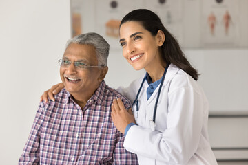 Optimistic older Indian man and happy young Brazilian doctor posing in examination room looking...