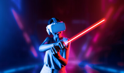 Naklejka premium Smart female standing wearing VR headset connecting metaverse, future cyberspace community technology. Elegant woman firmly holding laser saber seriously while play sword-fighting game. Hallucination.