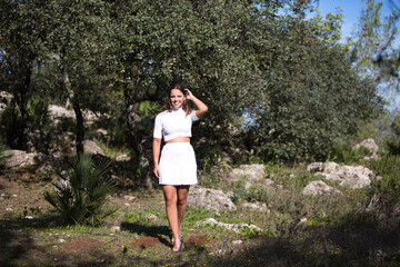 Beautiful brunette Latin woman walks among trees in a park while doing different facial and body...