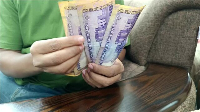 A young entrepreneur sitting in a corporate environment is counting  money.