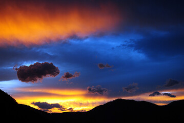 Brilliant Sunset in the Mountains: Orange and Blue Colors Envelop Detailed Clouds in a Natural Spectacle.