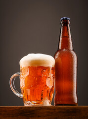 A bottle of beer and a glass of beer on a dark background.
