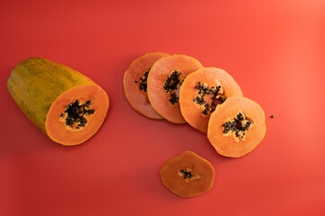 In the foreground, you see neatly sliced papaya resting on a vibrant red surface, while a whole, uncut papaya sits in the background, adding to the colorful display