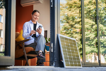 Happy woman using smartphone connected to photovoltaic solar panel. Integration of sustainable...