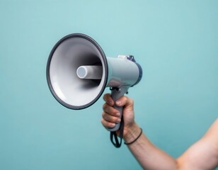 Close-up of a person holding a megaphone against a light turquoise background, conveying a message or announcement.