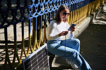Happy woman connecting smartphone to photovoltaic solar panel. Integration of sustainable renewable...