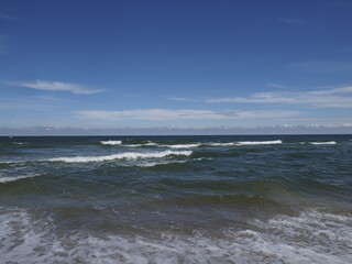 Calm sea with waves under a blue sky with white clouds on the horizon on a summer day