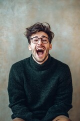 Obraz premium A joyful man wearing glasses and a dark green sweater is laughing heartily against a textured backdrop. Happy vibes!