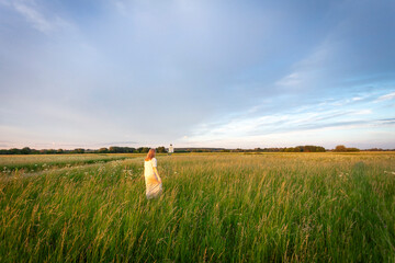 A white long-haired girl walks through a blooming meadow