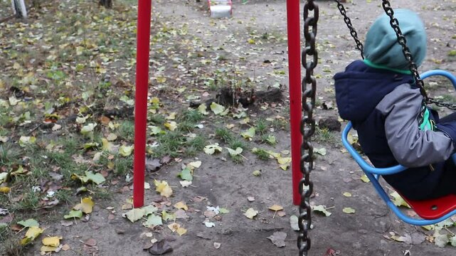 A little boy rides on an old swing on the playground