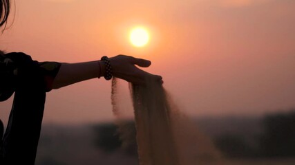 Sunset silhouette shot of desert sand falling from Indian woman's hand at Thar desert, Jaisalmer, Rajasthan, India. Sunset sky and desert sand. Travel and holidays concept.