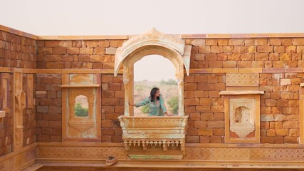 Indian Woman looking out of the window in old Rajasthani fort in Jaisalmer, India. Woman exploring old Khaba fort and haveli in Jaisalmer during  culture trip to India. 