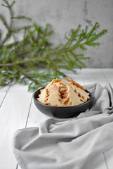 Omelette shortbread cookies with sugar in a white plate on the foreground and in a deep black one on the back. A large branch of a fir tree at the back. Vertical location.