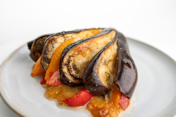 A plate of food with a variety of vegetables, including peppers and eggplant. The dish is served on a white plate and he is a healthy and colorful meal.