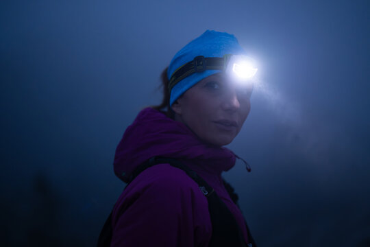 female Hiker or triathlon trail runner with a headlamp on a trail in the mountain with fog at night